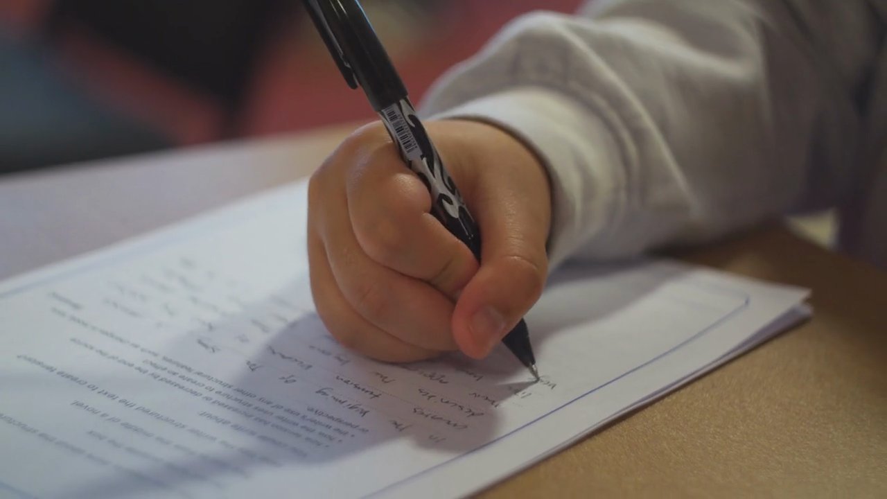 A learner handwriting answers on an exam paper